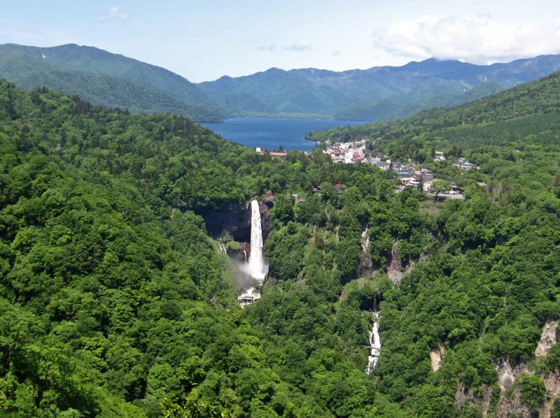 View over green forest to Kegon Falls with Lake Chuzenji and mountains behind