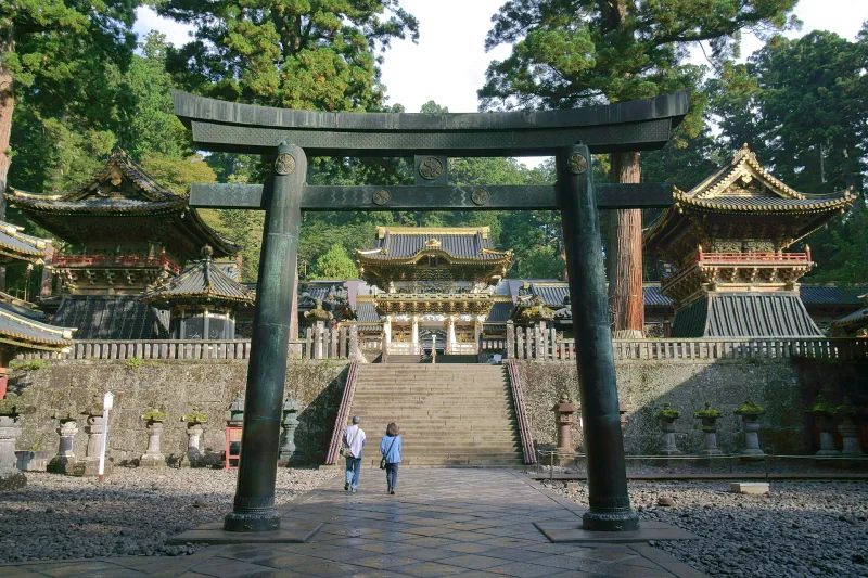 Bronze torii gate with the Yomeimon Gate and shrine buildings behind it in the forest