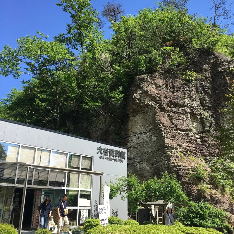 Entrance building of the Oya History Museum below a rocky, tree-covered hill