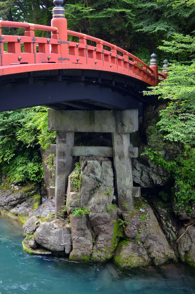 Stone pier and wooden beams under the red Shinkyo Bridge above the river