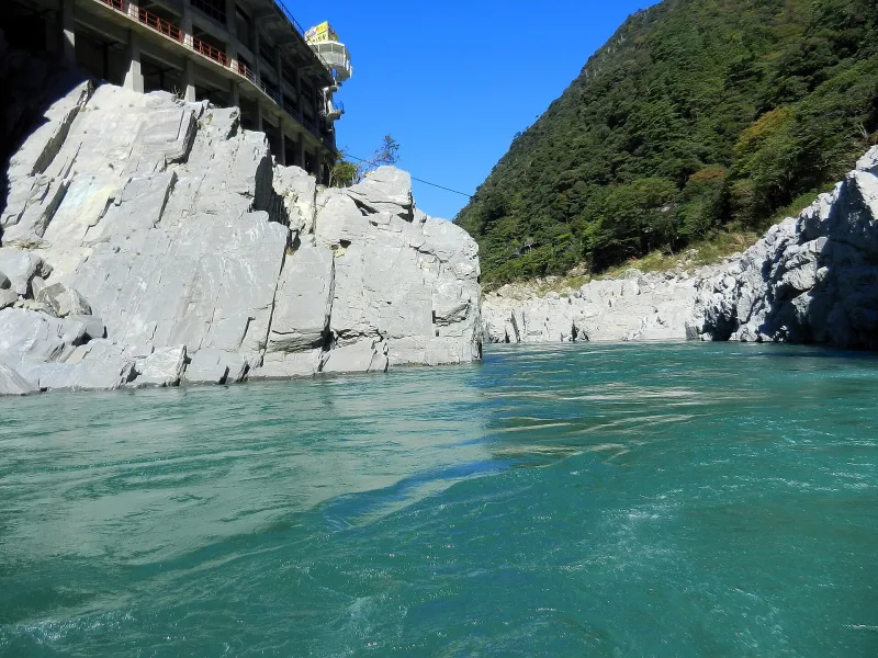 A large pale rock face rising from the emerald water of Oboke Gorge