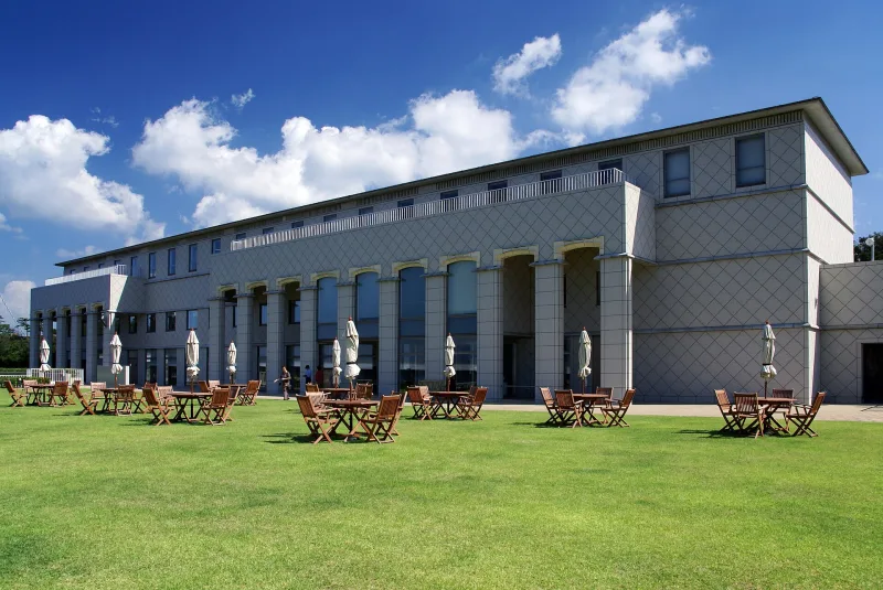 The museum's stone-clad building and lawn with outdoor tables under a blue sky