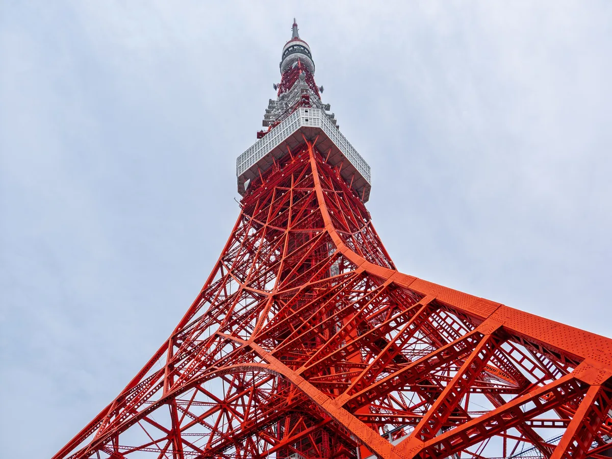 Looking up at the orange and white steel lattice of Tokyo Tower against a pale sky