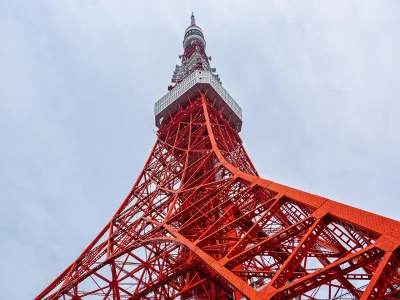 Looking up at the orange and white steel lattice of Tokyo Tower against a pale sky