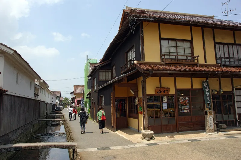 The narrow Tamagawa canal beside old white walls and a traditional wooden shopfront in Kurayoshi