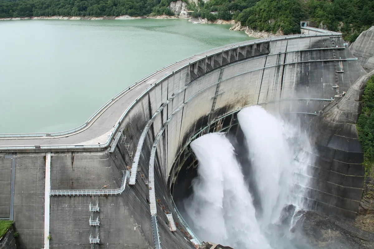 Kurobe Dam releasing a huge spray of water from its curved concrete wall beside a turquoise lake