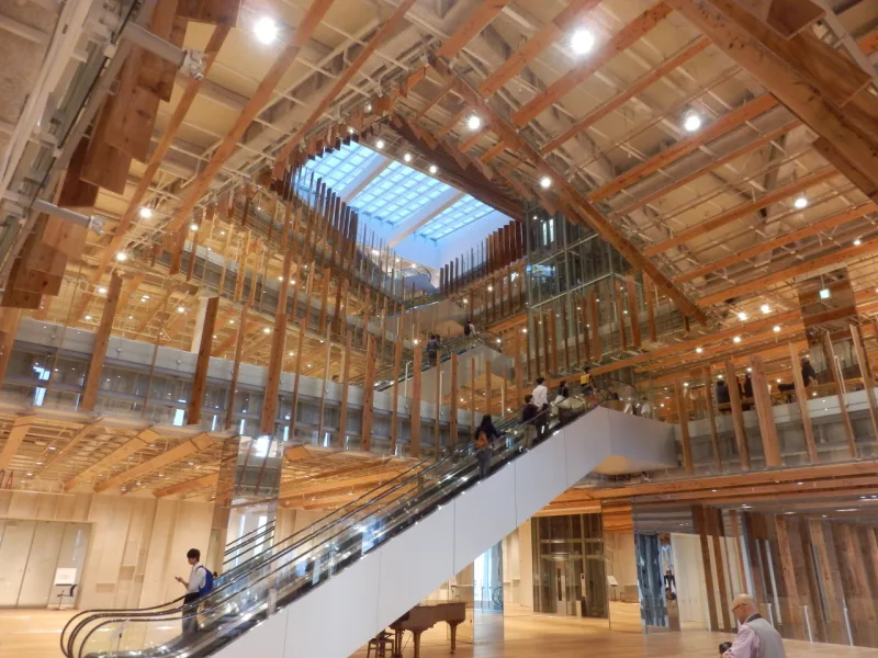 Atrium of TOYAMA Kirari lined with wooden louvers and escalators, lit by a skylight