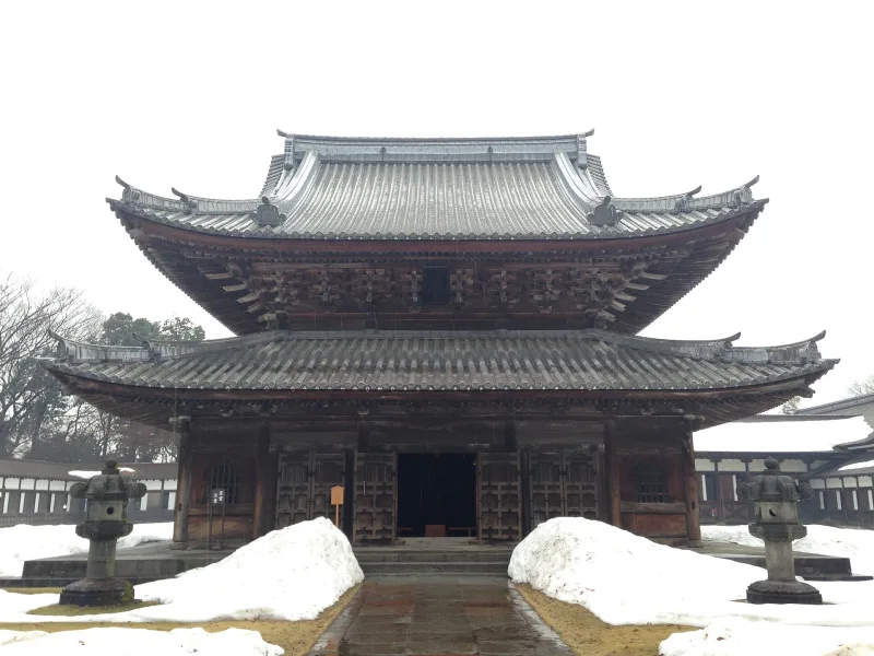 The Buddha hall of Zuiryuji Temple in snow, with stone lanterns