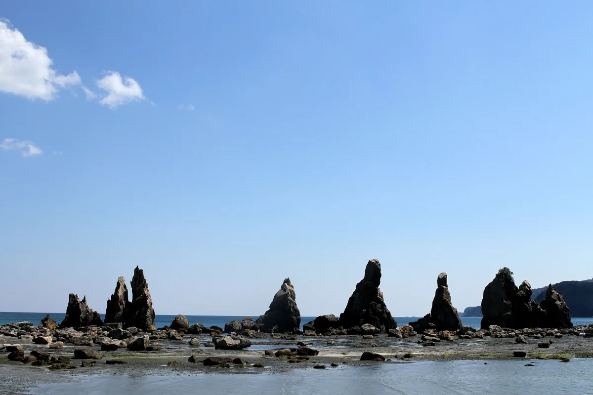 A straight line of tall rock pillars rising from the sea at Hashigui-iwa under a blue sky