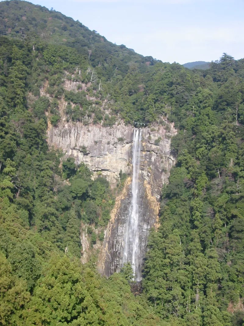 Distant view of Nachi Falls on a rocky cliff face surrounded by forested mountains