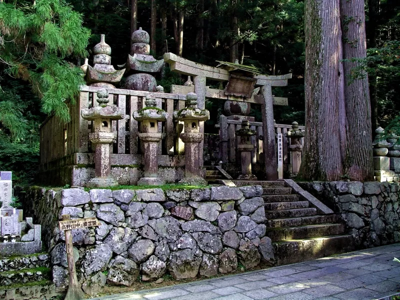 Old stone lanterns, a torii and grave monuments on a stone terrace in the Okunoin forest
