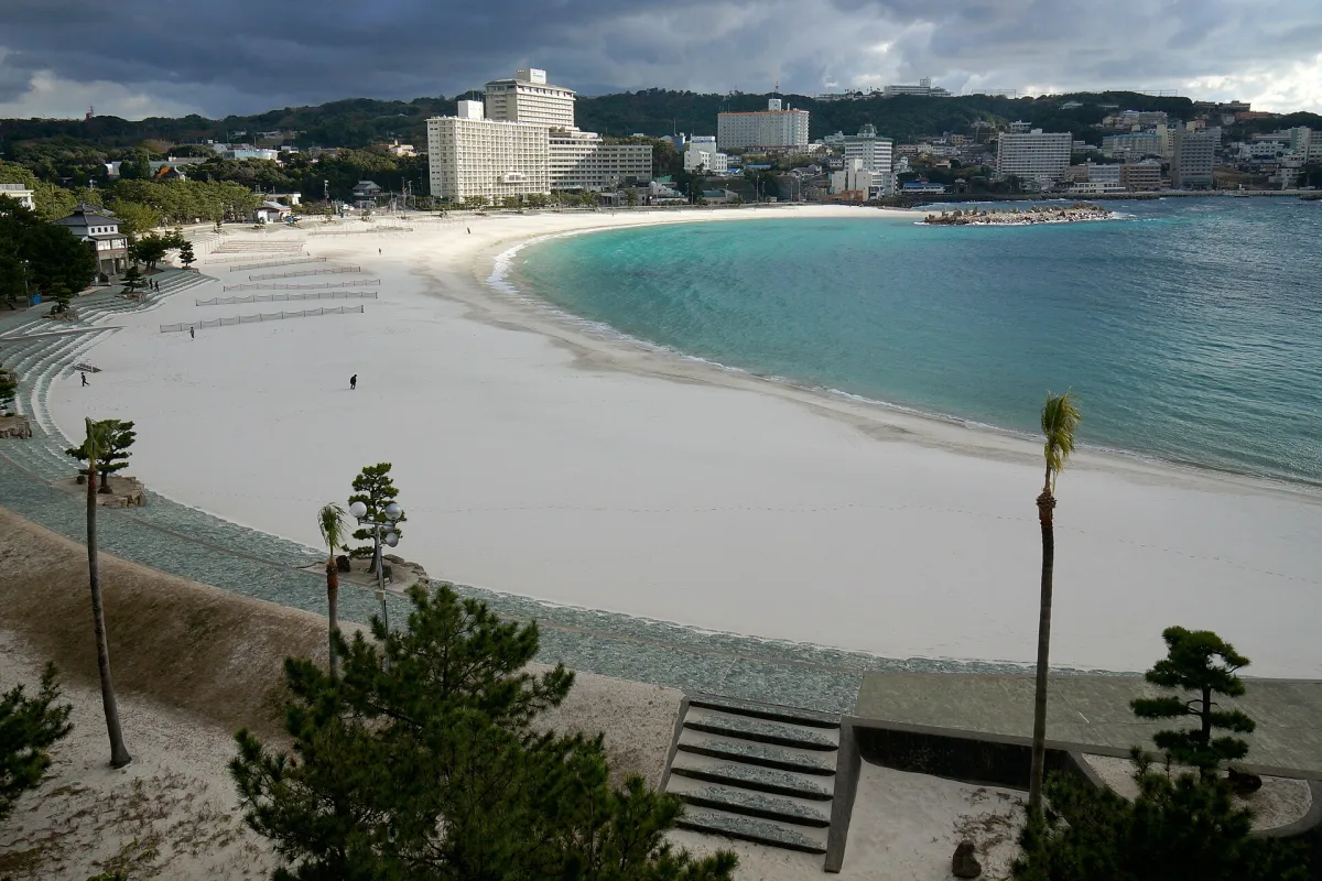 The curving white sand of Shirarahama Beach beside turquoise water, with hotels on the hills behind