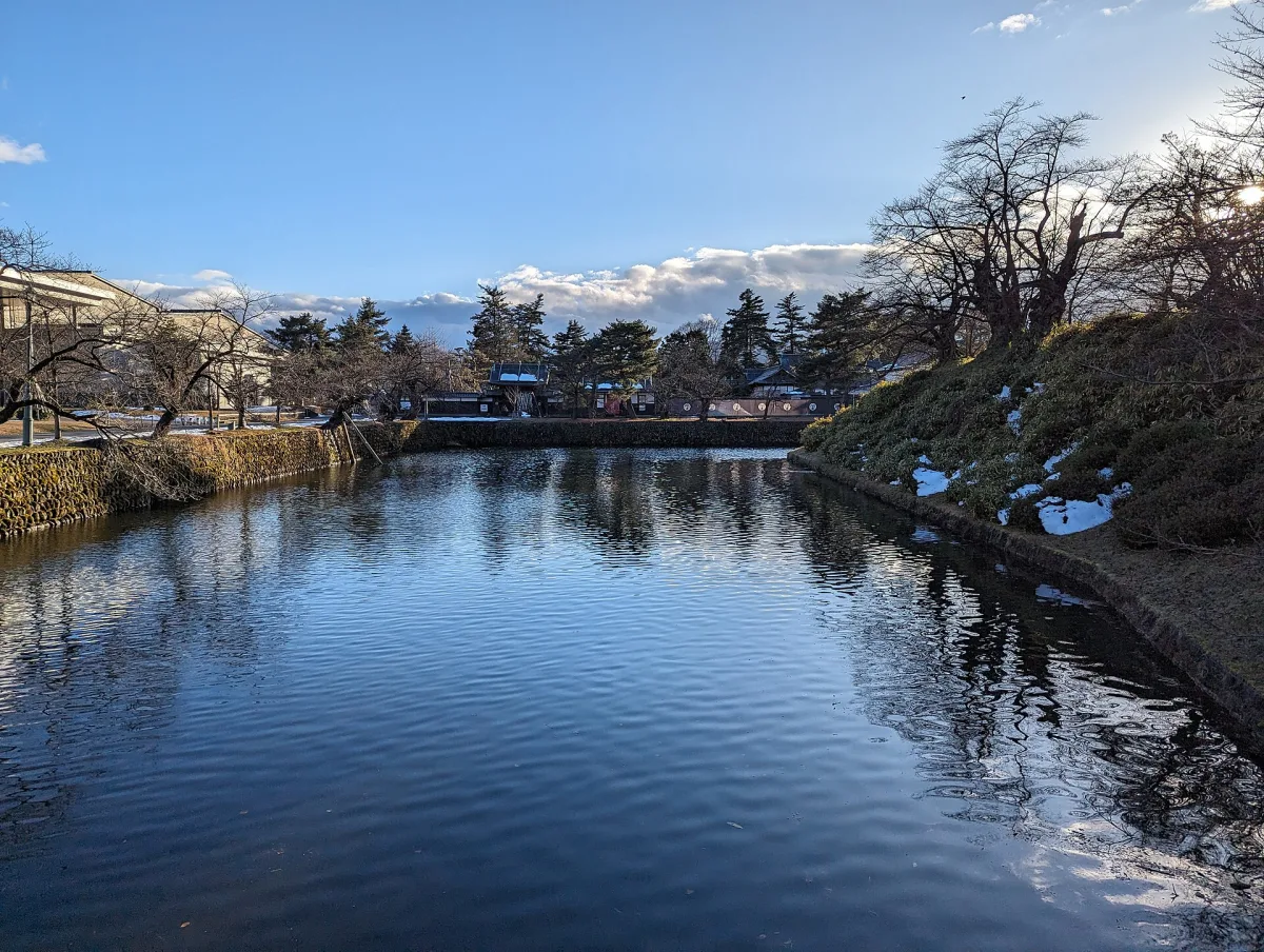 Water-filled moat of the former Yonezawa Castle with bare trees and patches of snow