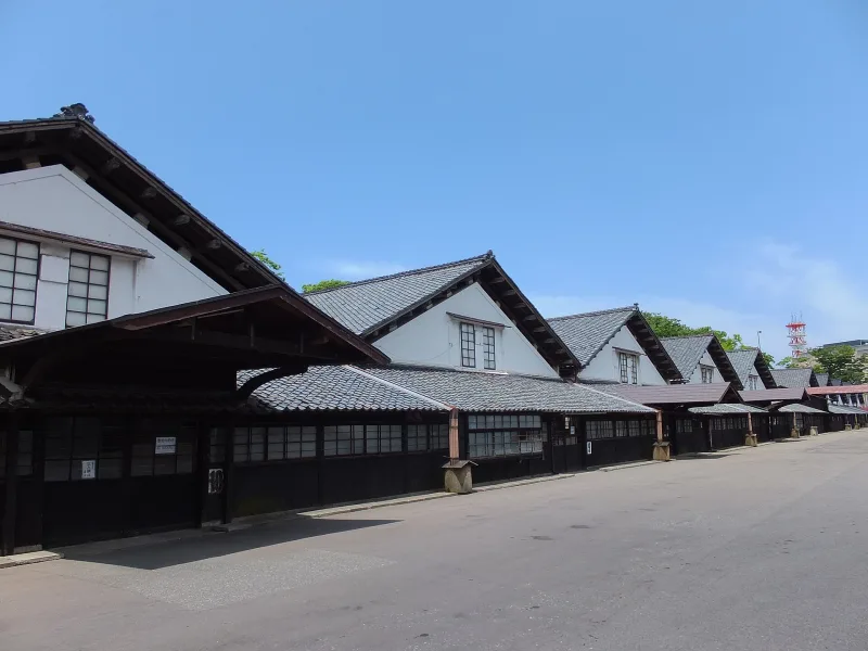 Row of white-walled rice warehouses with tiled roofs under a blue sky in Sakata