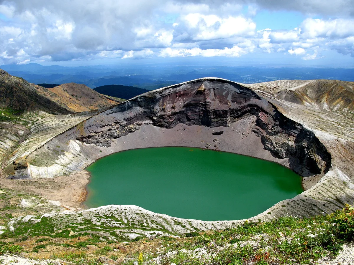 Emerald-green Okama crater lake ringed by grey volcanic walls on Mount Zao