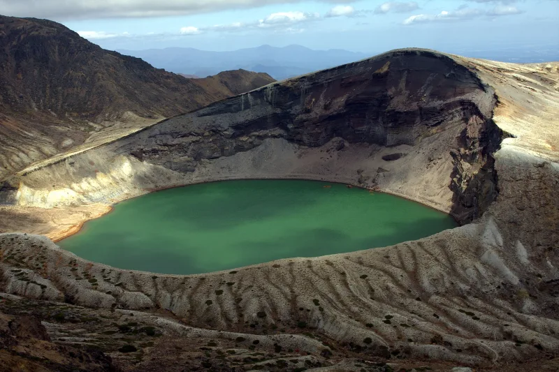 Okama crater lake on Mount Zao with striped volcanic slopes around the green water