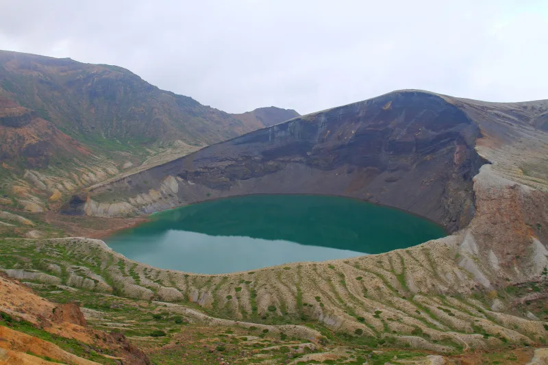 Turquoise Okama lake in its crater with autumn-coloured slopes of Mount Zao