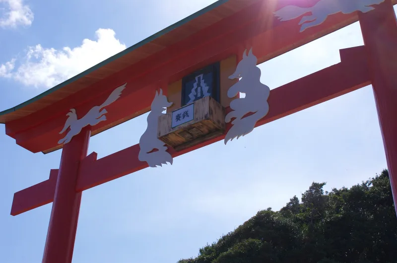 Looking up at the large red torii with the small offering box fixed high on its crossbeam