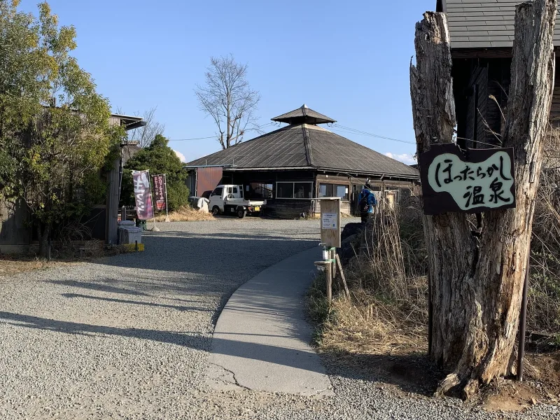 Entrance path to Hottarakashi Onsen with a wooden sign and a low building behind