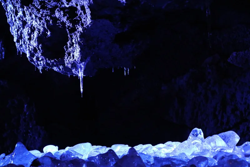 Blocks of ice lit in blue under a rough lava ceiling in Narusawa Ice Cave